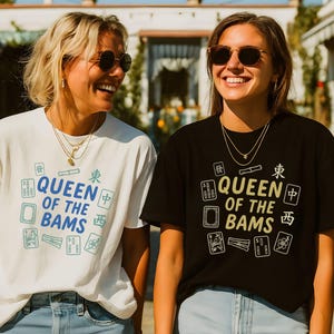 May include: Two women wearing t-shirts with the text "QUEEN OF THE BAMS" and Mahjong tile graphics. One shirt is white, the other black. Both women are smiling and wearing sunglasses and necklaces.