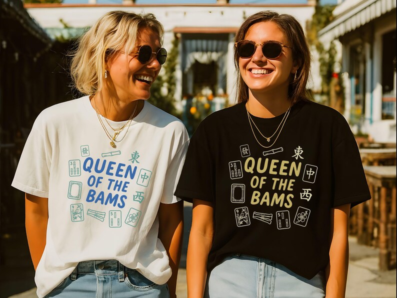 May include: Two women wearing t-shirts with the text "QUEEN OF THE BAMS" and Mahjong tile graphics. One shirt is white, the other black. Both women are smiling and wearing sunglasses and necklaces.