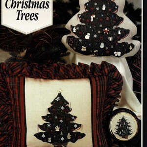 May include: A cross stitch pattern book titled "Treasured Christmas Trees" by Mill Hill. The cover features a black and white cross stitch design of a Christmas tree with ornaments and a snowman. The tree is on a white pillow with a red and black plaid border.