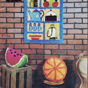 May include: Latch hook patterns for a kitchen cupboard wall hanging, orange pillow, watermelon pillow, and wall clock hanging. The patterns are shown with completed projects, including a blue and yellow kitchen cupboard, a bright orange pillow, and a watermelon pillow.