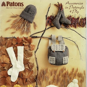 May include: A collection of knitted items: a grey beanie, socks, a backpack, and a white cable-knit hat and scarf set. The image includes dried wheat, leaves, and small pumpkins. Text reads "Accessories in Patonyle 4 Ply".