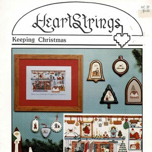 May include: A Christmas-themed cross-stitch pattern with the text "HeartStrings Keeping Christmas." The image features a framed cross-stitch scene, decorative ornaments, and a Santa Claus figure. The color palette includes red, green, and brown.