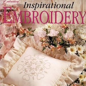 May include: A cream-colored pillow with an embroidered floral design, surrounded by lace trim and ruffled edges. The image features the text "Inspirational Embroidery" and "18 Gorgeous projects Pattern sheet included". Flowers and ribbons are also present.