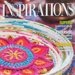 Puede incluir: La portada de la revista de bordado "Inspirations" presenta un dise&ntilde;o bordado colorido. El t&iacute;tulo de la revista est&aacute; en la parte superior, con texto que destaca estudios bot&aacute;nicos, bordado sobre organza y girasoles stumpwork. La frase "A Feast for the Needle" est&aacute; en la parte inferior.