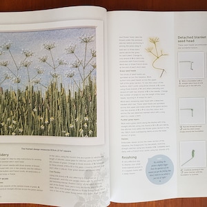 Puede incluir: Un libro abierto muestra un proyecto de bordado de una escena de pradera. El dise&ntilde;o enmarcado mide 8,5 cm cuadrados. El bordado presenta hierba verde alta, flores blancas y un fondo de cielo azul. Tambi&eacute;n se muestran instrucciones y diagramas para el bordado.