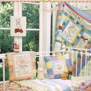 May include: A baby's cot with a patchwork quilt, cushions, and a framed cross-stitch. The quilt and cushions feature pastel colours and bunny designs. The text "Little Chicken Feather & Friends" is at the top, with "Making room for baby..." at the bottom.
