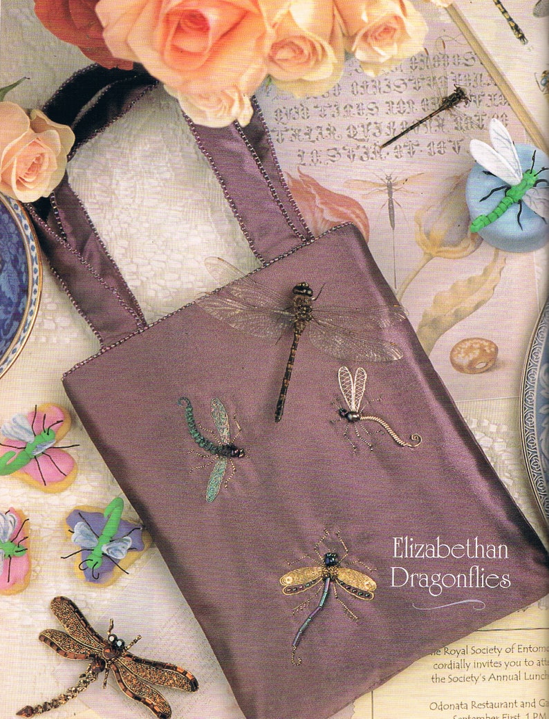 May include: A purple satin bag with beaded trim and embroidered dragonflies. The bag has two handles and is decorated with a variety of dragonfly designs. The text "Elizabethan Dragonflies" is printed on the bag.