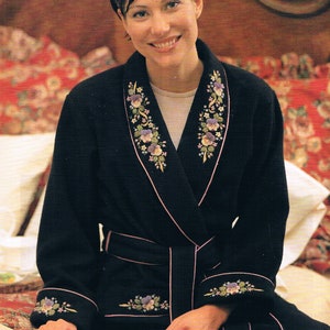 May include: A black robe with a pink trim and floral embroidery. The robe has a shawl collar and a sash tie. The embroidery features small purple flowers and green leaves.