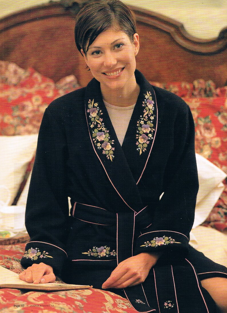 May include: A black robe with a pink trim and floral embroidery. The robe has a shawl collar and a sash tie. The embroidery features small purple flowers and green leaves.