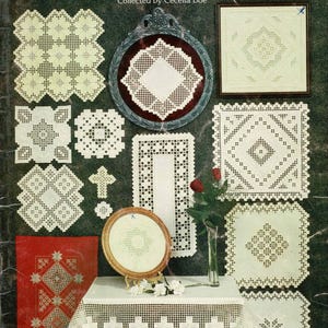 May include: An assortment of Hardanger embroidery pieces, including framed examples, a table runner, and a tablecloth with a decorative edge. The image showcases white-on-white designs, a cross, and a vase of red roses. The title reads "Family Traditions In Hardanger Embroidery."