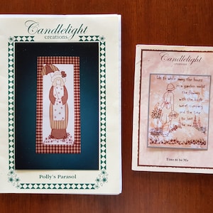 May include: Two cross-stitch patterns from Candlelight Creations. The first pattern features a woman with an umbrella and the text "Polly's Parasol". The second pattern features a woman in a garden with the text "Oh to while away the hours in a garden midst the flowers with the buds sweet company and the time to just be me" and "Time to be Me".
