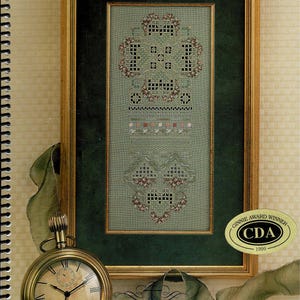 May include: A framed cross-stitch sampler on sage green fabric with intricate geometric and floral patterns, displayed with a gold pocket watch, a thimble, and scissors. The sampler features the text "CROSS 'N PATCH" and "The Unfinished Sampler".