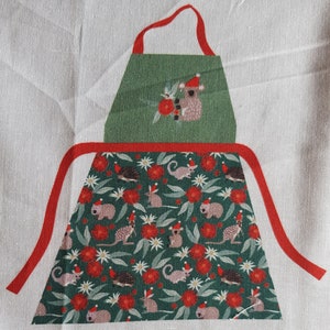 May include: Green and red Christmas-themed apron with a koala wearing a Santa hat on the top pocket. The apron has a repeating pattern of koalas, echidnas, and gum leaves.