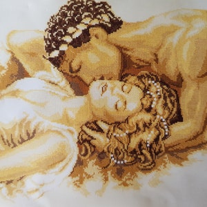 May include: A cross-stitch embroidery depicting a couple embracing. The man is on top of the woman, with his arm around her waist. They are both wearing simple clothing and have their eyes closed. The embroidery is done in shades of brown and beige.