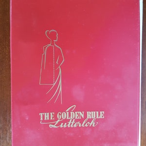 May include: Red folder with a gold outline of a woman in a dress and the text "THE GOLDEN RULE Lutterloh" in gold.