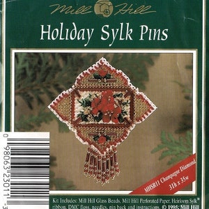 May include: A kit for making a Holiday Sylk pin. The pin is diamond-shaped with red floral and bead embellishments. The kit includes beads, perforated paper, ribbon, floss, needles, and instructions. The text "Holiday Sylk Pins" is at the top.