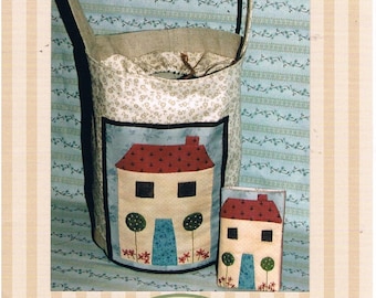 May include: A French Cottage Set sewing pattern by The Birdhouse Patchwork Designs. The pattern includes a tote bag and a small pouch, both featuring a charming cottage design with a red roof, blue door, and green trees. The tote bag has a brown handle and a white background with a floral pattern.