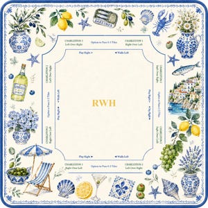 May include: A decorative square tablecloth with a blue and white border, featuring illustrations of lemons, olives, sardines, and coastal scenes. The center has the letters "RWH" in gold. Includes images of a beach umbrella, a cocktail, and a bottle of Limoncello.