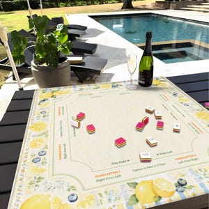 Pu&ograve; includere: Un gioco da tavolo con un design a limone e mirtillo, con pedine rosse, rosa e bianche. Una bottiglia di champagne e un bicchiere sono sul tavolo. Il tabellone di gioco riporta la scritta "CHARLESTON 1" e "CHARLESTON 2".