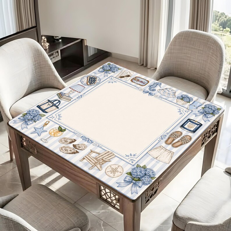 May include: A square wooden table with a nautical-themed design. The tabletop features a cream-colored center surrounded by a blue and white striped border with illustrations of seashells, hydrangeas, and beach accessories.