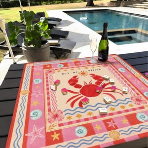 K&ouml;nnte beinhalten: Ein farbenfrohes Spielbrett im Strand-Design mit einer gro&szlig;en roten Krabben-Illustration und dem Text "OUT OF OFFICE". Das Spielbrett hat ein rosa-cremefarbenes Farbschema mit Seesternen, Muscheln und Hibiskusbl&uuml;ten. Mehrere Spielsteine sind darauf verstreut.