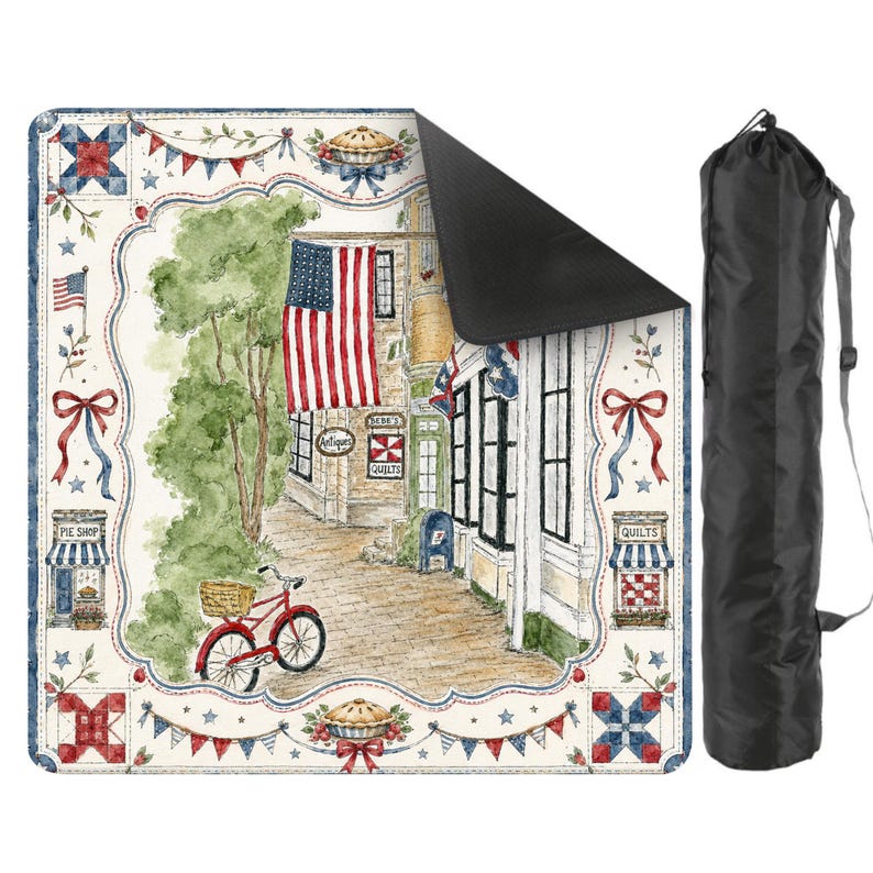 May include: A picnic blanket with a patriotic design, showing a watercolour illustration of a charming American town with an American flag, a red bicycle, and a pie shop. Includes a black carry bag.