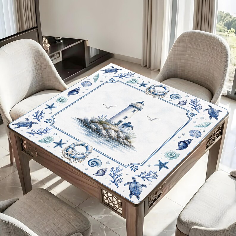Puede incluir: Mesa cuadrada de madera con dise&ntilde;o n&aacute;utico. La superficie presenta una ilustraci&oacute;n de faro rodeada de conchas marinas, estrellas de mar y tortugas en tonos azules y blancos. La mesa tiene un marco de madera y est&aacute; rodeada de sillas.