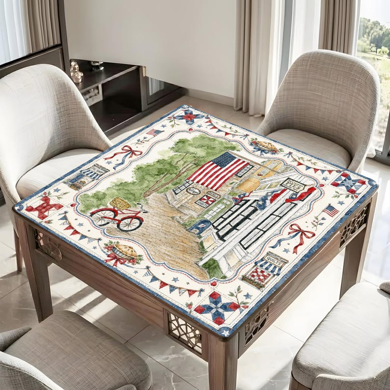 May include: A square wooden table with a decorative top featuring a watercolour illustration of an American town scene. The design includes an American flag, a red bicycle, and patriotic elements. The table is surrounded by chairs.