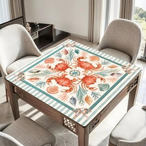 May include: A square wooden table with a nautical-themed design. The tabletop features a cream-colored background with a border of teal stripes. The design includes orange crabs, seashells, and a compass rose. The table has four legs and decorative cutouts.