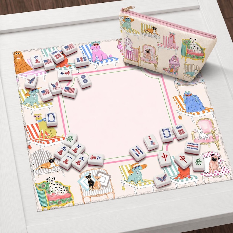 May include: A pink and white mahjong set with dog illustrations, including a matching zippered pouch. The set features tiles with various symbols and American flag designs. The mat has a pink center with a green and pink border.