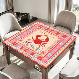 K&ouml;nnte beinhalten: Ein quadratischer Tisch mit einem Krabbenmuster. Der Tisch hat ein rotes, rosa und beiges Krabben- und Ozeanmuster. Der Text "out of office" ist auf den Tisch gedruckt. Der Tisch ist aus Holz und hat eine dekorative Kante. Ca. 80 cm x 80 cm.