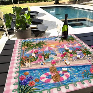 May include: A decorative table mat with a beach scene design, featuring dogs, palm trees, and a pool. The mat has a pink and white gingham border. A bottle of champagne and a glass are on the table. The scene evokes a holiday atmosphere.