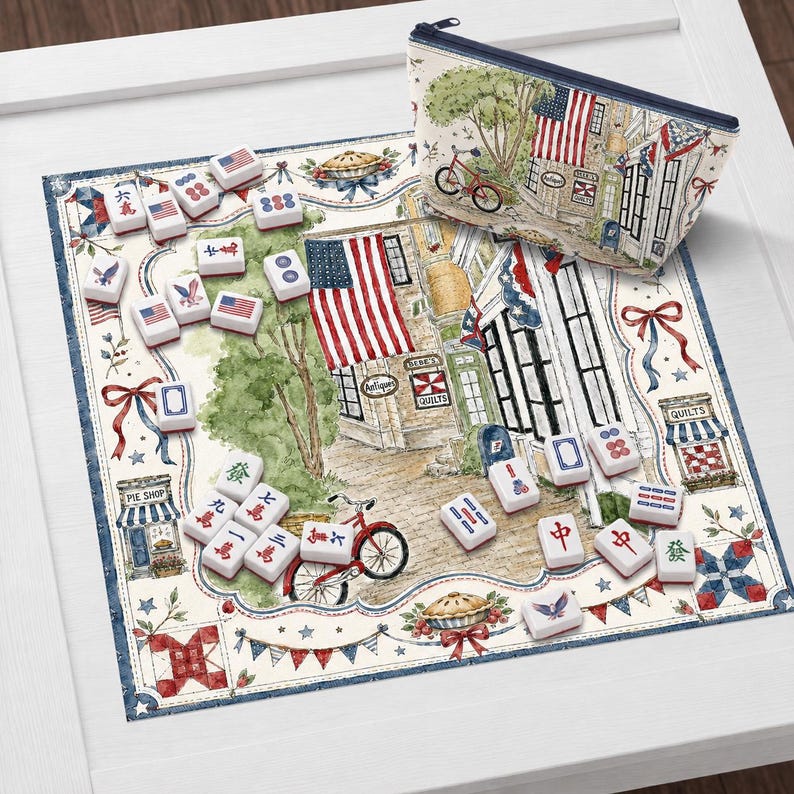 May include: A mahjong set with red, white, and blue tiles, a matching zippered pouch, and a printed mat featuring an Americana scene with flags, shops, and a bicycle. The set is displayed on a white surface.
