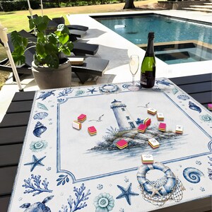 Puede incluir: Una mesa de tem&aacute;tica n&aacute;utica con un mantel individual blanco y azul con un faro, conchas marinas y estrellas de mar. Una botella de champ&aacute;n y una copa est&aacute;n sobre la mesa, junto con piezas de juego coloridas. La escena est&aacute; ambientada al aire libre, cerca de una piscina.