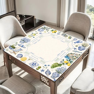 May include: A wooden table with a decorative top featuring a coastal design. The design includes illustrations of lemons, seashells, and blue and white pottery. The table is surrounded by chairs and has a light-colored surface with a border.