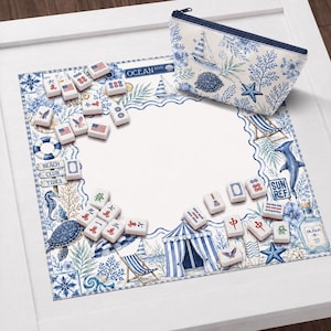 May include: A decorative white Mahjong set with blue and red accents, featuring a beach theme. Includes a matching zippered pouch with a sailboat design. The set is arranged on a white surface with beach-themed illustrations.