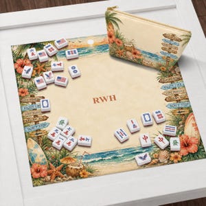 K&ouml;nnte beinhalten: Mahjong-Set mit Strandmotiv. Das Set enth&auml;lt Spielsteine, eine Spielmatte und eine Rei&szlig;verschlusstasche. Die Spielmatte zeigt eine Strandszene mit Palmen, einem Surfbrett und den Buchstaben "RWH". Die Tasche hat eine Strandszene und die Worte "Enjoy Life".