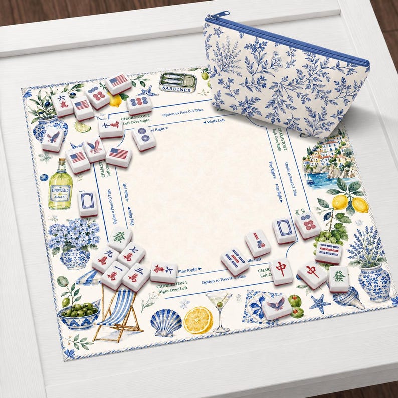 May include: A decorative Mahjong game set with a blue and white floral print cosmetic bag. The game board features a coastal design with lemons, olives, and a beach scene. The Mahjong tiles are white with red and blue markings.