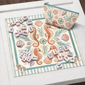 May include: A Mahjong set with a marine theme, featuring seahorses, seashells, and a compass rose design. The set includes tiles with various symbols and a matching zippered pouch. The background is a patterned mat with a striped border.