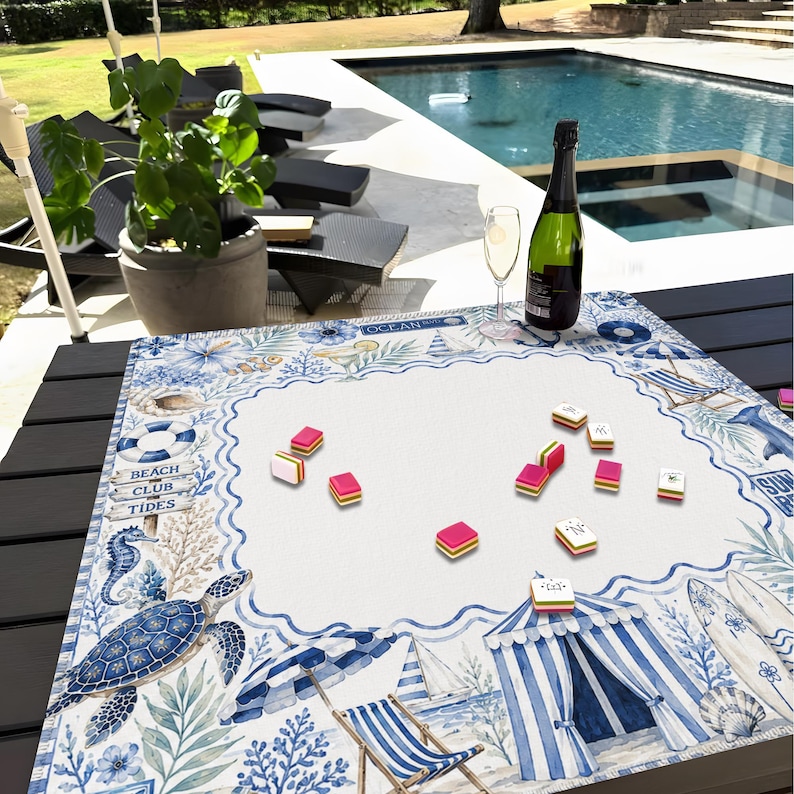 May include: A beach-themed game board with a white center and a blue and white border featuring illustrations of a turtle, seahorse, and beach chairs. The board has the text "Beach Club Tides" and is surrounded by game pieces, a bottle of champagne, and a glass.