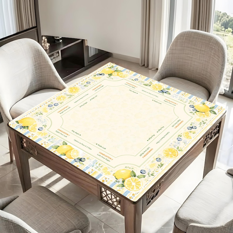 Pu&ograve; includere: Un tavolo in legno con un piano decorativo a motivi di limoni e mirtilli. Il tavolo ha uno sfondo giallo chiaro con un bordo di limoni, mirtilli e testo. Il tavolo &egrave; circondato da tre sedie grigie.