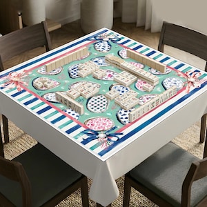 May include: A square tablecloth with a teal background featuring a pattern of blue and white patterned plates, pink floral accents, and blue ribbons. The border consists of blue and white stripes. Mahjong tiles are arranged on the surface of the cloth.