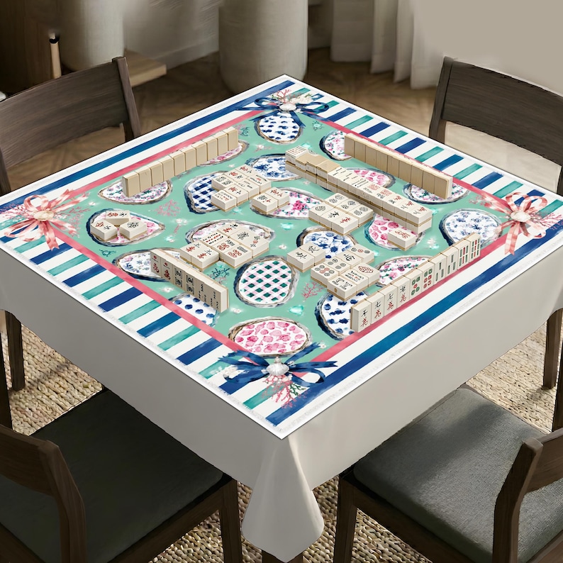 May include: A square tablecloth with a teal background featuring a pattern of blue and white patterned plates, pink floral accents, and blue ribbons. The border consists of blue and white stripes. Mahjong tiles are arranged on the surface of the cloth.