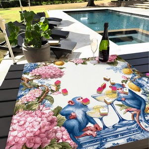 May include: A decorative table runner featuring a whimsical design with blue monkeys, cocktails, and pink hydrangeas. The runner has a white background with blue and pink floral accents, and is adorned with colorful candies and lemons.