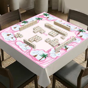 May include: A square mahjong mat featuring a white center and a pink border decorated with illustrations of palm trees and water. The mat is laid out on a table with several sets of mahjong tiles arranged in rows and small groups across the surface.