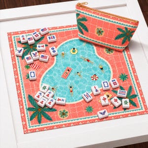 May include: A mahjong set featuring a rectangular zippered pouch with a coral and palm tree print, and a matching game mat depicting a swimming pool scene with swimmers. The set includes white tiles with various symbols, American flags, and birds.