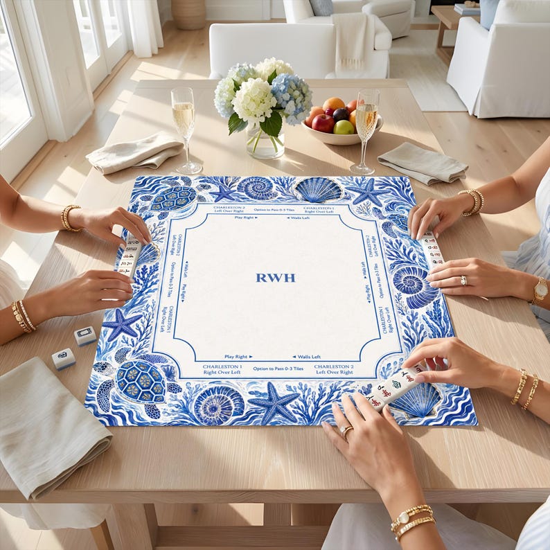 May include: A square mahjong mat featuring a blue and white coastal pattern with sea turtles, starfish, and seashells. The center is white with the letters RWH in blue, surrounded by game instructions and directional arrows for play.