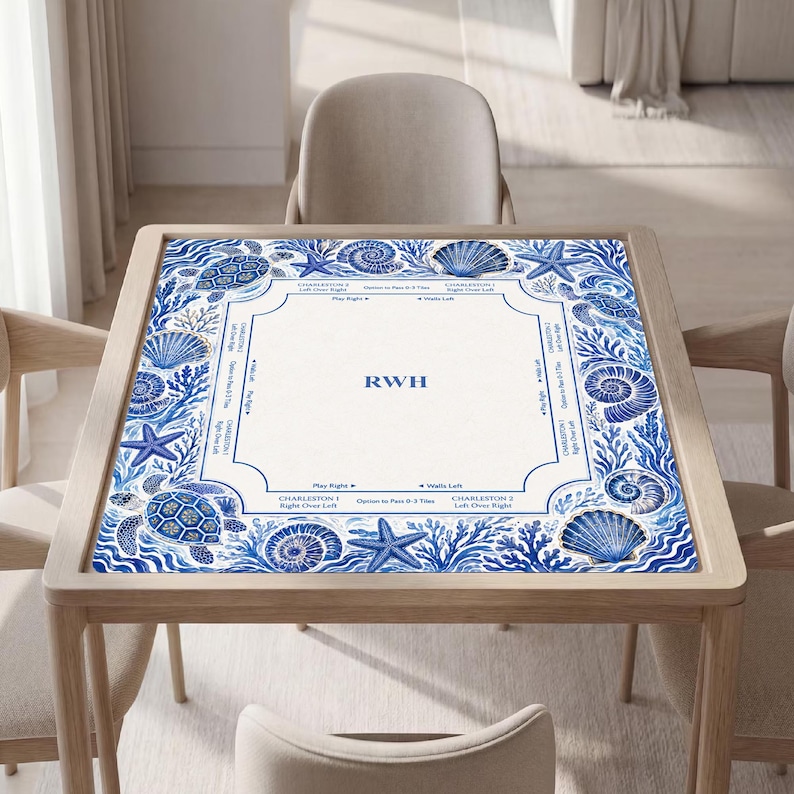 May include: A square mahjong mat featuring a white center with the letters RWH and game instructions, surrounded by a blue and white border decorated with illustrations of sea turtles, starfish, seashells, and coral reef patterns.