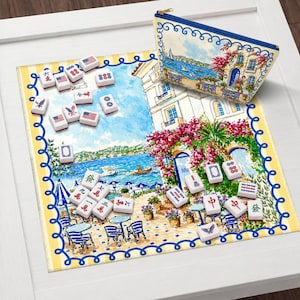Puede incluir: Un juego de Mahjong decorativo con una bolsa con cremallera a juego. El juego incluye fichas con varios s&iacute;mbolos y dise&ntilde;os de la bandera estadounidense. La bolsa y la alfombra presentan una ilustraci&oacute;n costera esc&eacute;nica con detalles azules y rosas.