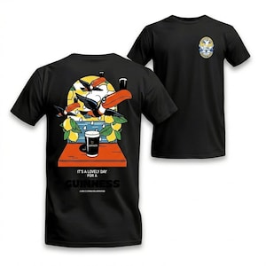 Puede incluir: Camisetas negras con un dise&ntilde;o tem&aacute;tico de Guinness. La parte delantera de la camiseta presenta un peque&ntilde;o emblema, mientras que la parte trasera muestra una colorida ilustraci&oacute;n de tucanes, limones y una pinta de Guinness, con el texto "It's a lovely day for a Guinness."